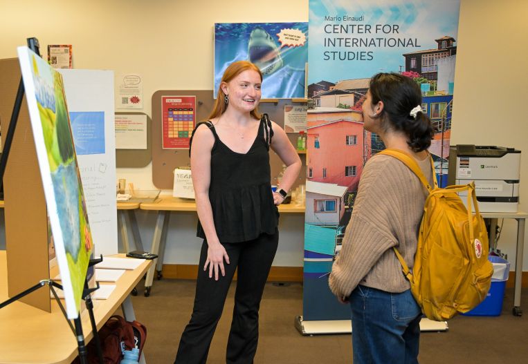 Global Scholar Mira DeGregory stands and talks with a student in front of her painting at the student showcase.